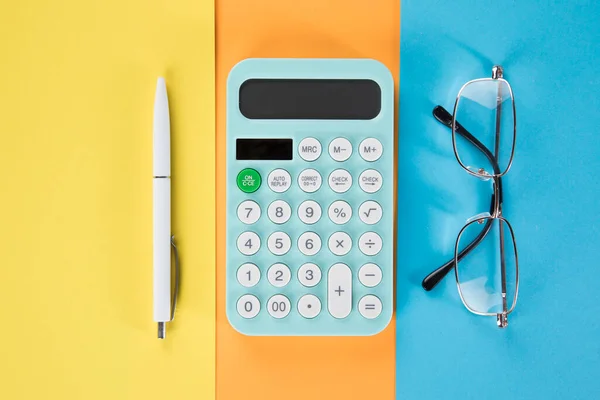 on the desktop calculator, pen and glasses. multicolored paper