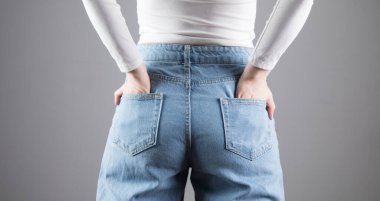 Kız ellerini arka cebine koydu. Gri bir arka planda.