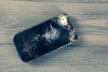 Gri ahşap bir masada kırık bir telefon.