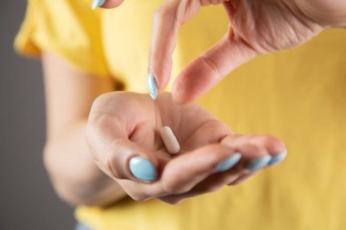 Sarı elbiseli bir kız elinde hap tutuyor.