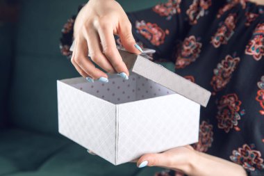 Elbiseli genç kız kanepede oturan hediye kutusunu açıyor.