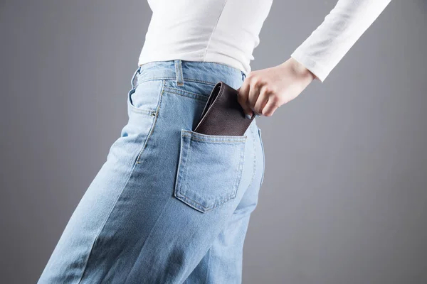 young woman pulls out her wallet from her pocket on a gray background