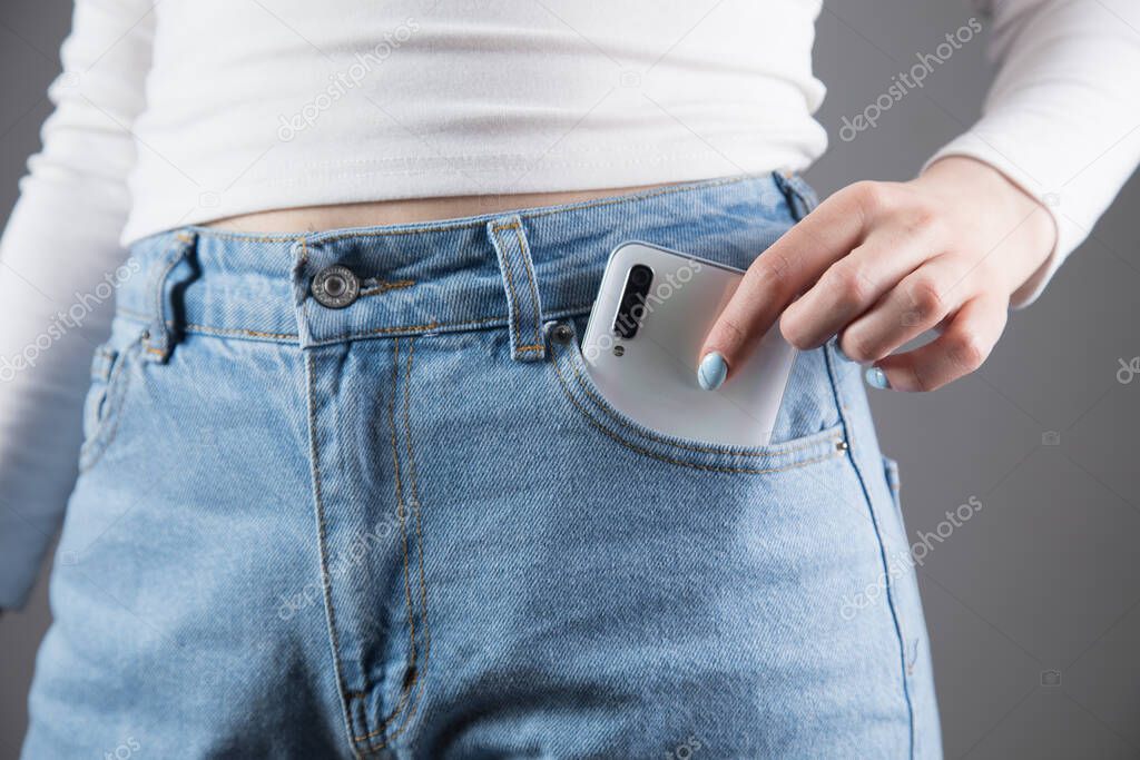 woman pulls out a phone from her pocket on a gray background