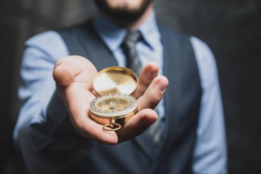 Gri arka planda altın pusula tutan takım elbiseli adam.