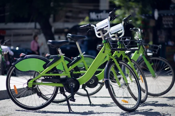 several green bicycles on the street. bicycles for rent