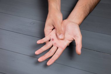 Bir adam gri arka planda nasır gösterir.