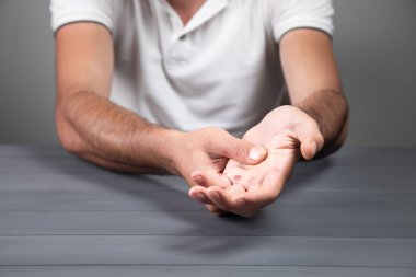 Bir adam gri arka planda nasır gösterir.