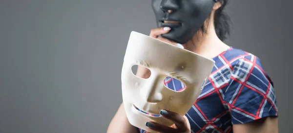 woman holding black and white plastic mask on gray background