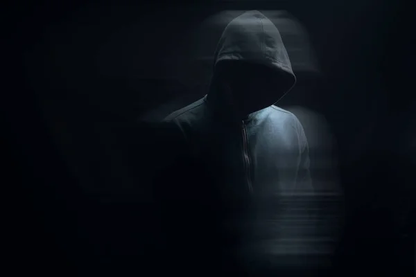 a man in a hood stands on a black background