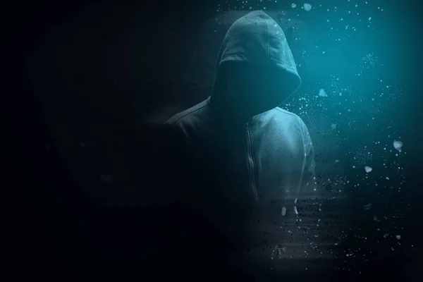 Kapüşonlu bir adam siyah arka planda duruyor.