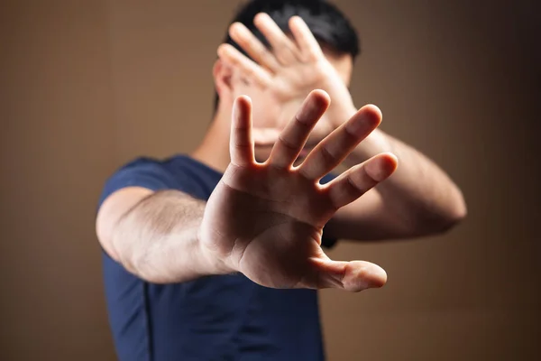 man hides his face with his hands on a brown background