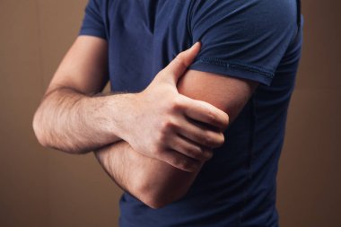 Genç adamın kahverengi arka planda yaralı bir kolu var.