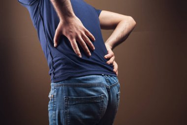 Bir adam kahverengi arka planda böbreklerine zarar verir.