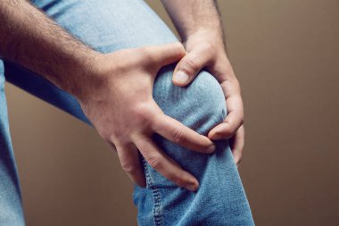 Kahverengi arka planda bir adamın diz ağrısı vardır.