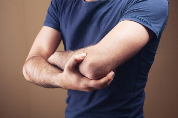 Ein Junger Kerl Hat Einen Schmerzenden Ellbogen Auf Braunem Hintergrund — Stockfoto