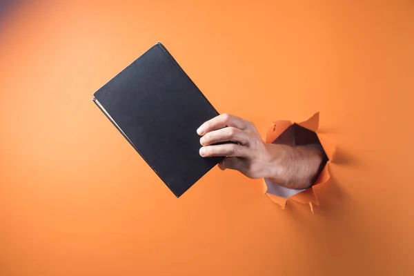 Hand holds book on orange background