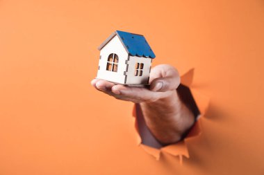 Turuncu arka planda bir evi tutan el.