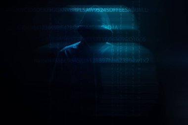 Kapüşonlu bir adam siyah arka planda duruyor.