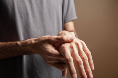 Kahverengi arka planda bileği ağrıyan bir adam.