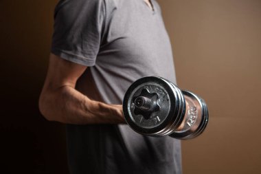 Kahverengi arka planda dambıllarla egzersiz yapan bir adam.