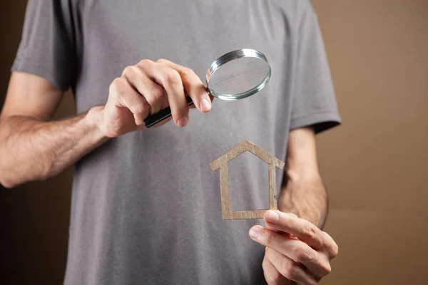 magnifying glass looks at the house. real estate search on brown background