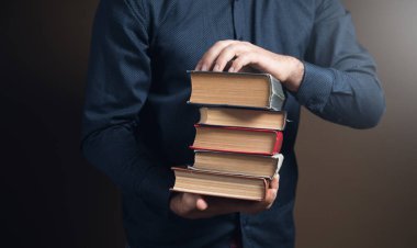 Kahverengi arka planda kitapları tutan bir adam.