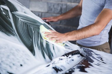 Adamın biri arabanın köpüğünü bez parçasıyla siliyor. araba yıkama