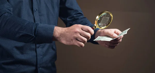 a man with a magnifying glass looks at money on a brown background