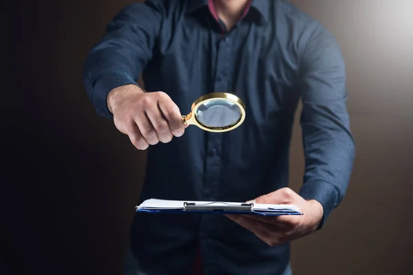 一个拿着放大镜的人看着褐色背景的文件 — 图库照片
