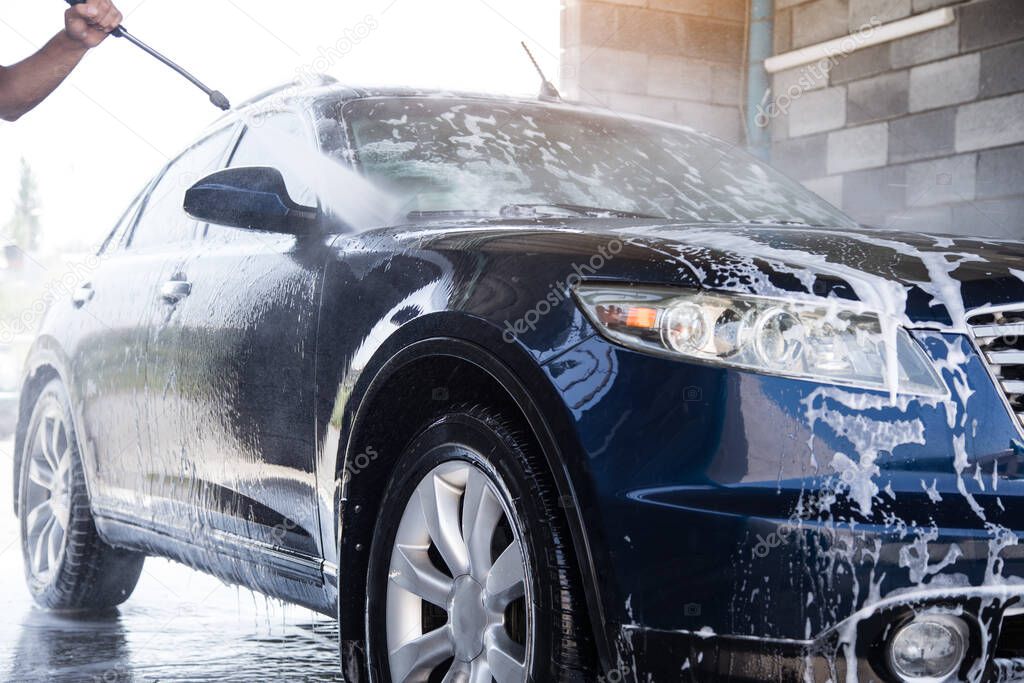 the man washes the foam out of the car with the pressure of water