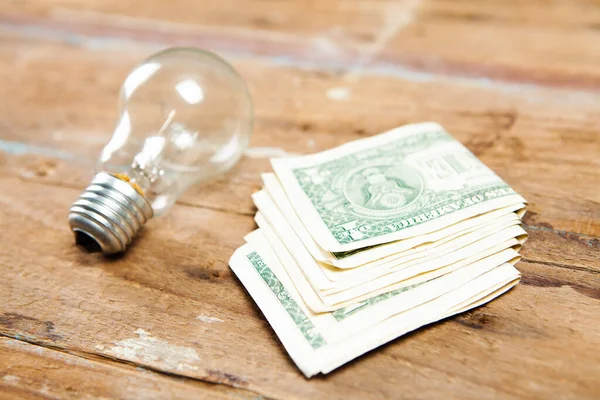 dollar bills and light bulb on wooden table