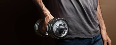 Kahverengi arka planda dambıllarla egzersiz yapan bir adam.