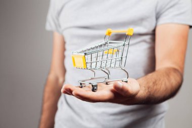 Bir adam elinde bir el arabası tutuyor. Gri arka planda alışveriş kavramı