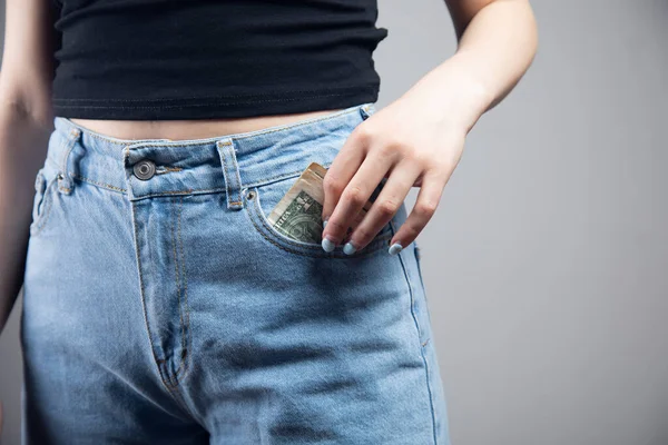 woman pulls money out of pocket on gray background
