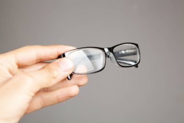 Gri arka planda optik gözlükleri tutan el.