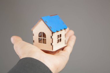 Gri arka planda bir evi tutan el.