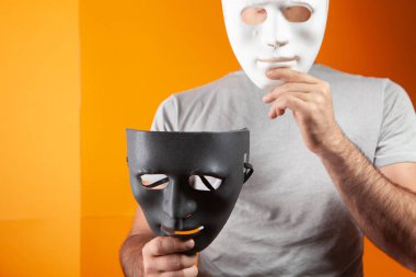 Turuncu arka planda siyah ve beyaz bir maske tutan bir adam.