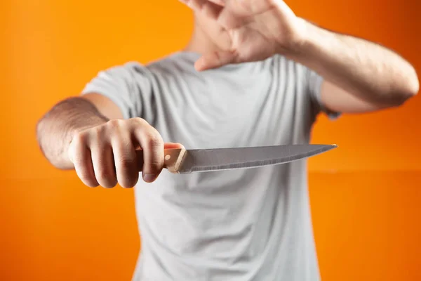一个男人站在橙色背景上拿着一把刀 — 图库照片