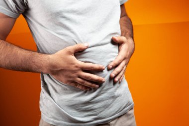 Adamın turuncu arka planda karnı ağrıyor.