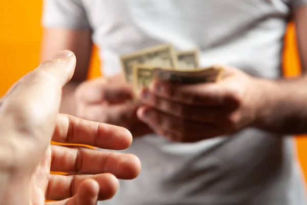 man holding money and giving to another on orange background