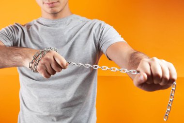 Turuncu arka planda elinde zincir tutan bir adam.