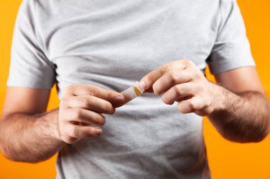 Adamın biri turuncu arka planda bandaj gösteriyor.