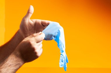 Adam turuncu arka plana lastik eldiven takıyor.