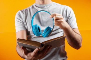 Bir adam elinde kitap ve kulaklıkla ayakta duruyor. auobook