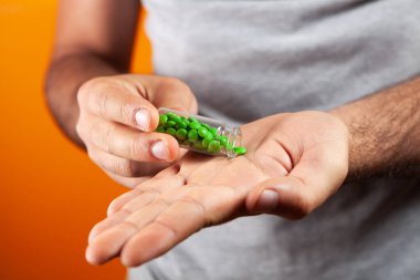 Turuncu arka planda hapları olan kapsülü tutan adam.