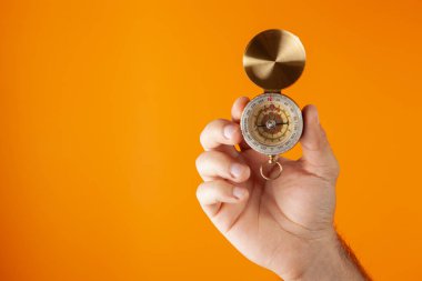 El, turuncu arka planda pusulayı tutar