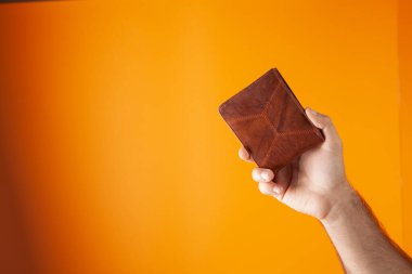 Cüzdanı turuncu arka planda tutuyor.