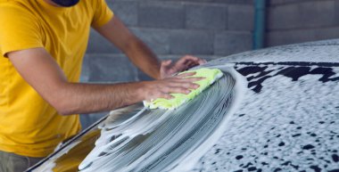 Adamın biri arabanın köpüğünü bez parçasıyla siliyor. araba yıkama