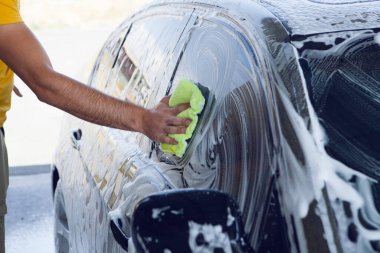 Adamın biri arabanın köpüğünü bez parçasıyla siliyor. araba yıkama