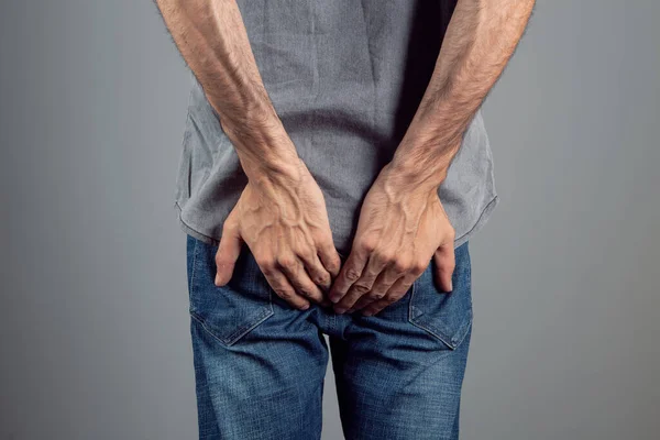 man with hemorrhoids holding ass on gray background